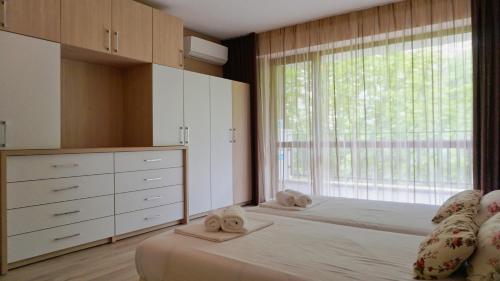 a bedroom with two beds and a large window at Апартамент Балчик Гардънс - Balchik Gardens Apartment in Balchik