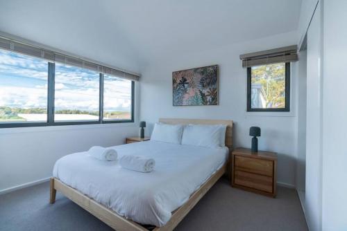 a white bedroom with a bed and two windows at Absolute waterfront beach house in Minnamurra