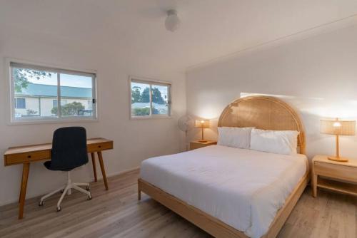 a bedroom with a bed and a desk and two windows at Absolute waterfront beach house in Minnamurra