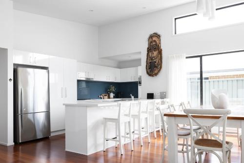 a white kitchen with a table and a refrigerator at Seagrass in Vincentia