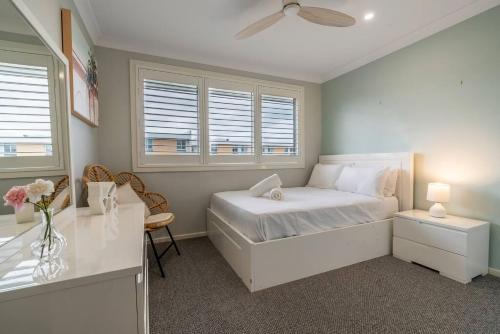 a white bedroom with a bed and a desk at Sea Change in Shellharbour