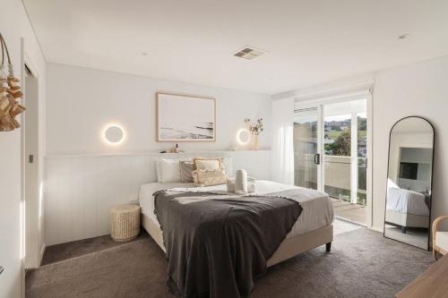a white bedroom with a bed and a mirror at The White Haven of Gerringong in Gerringong