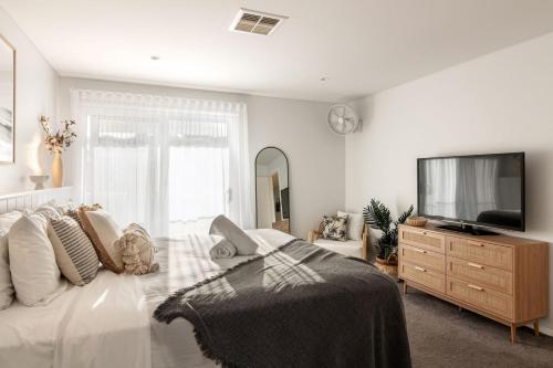 a white bedroom with a bed and a flat screen tv at The White Haven of Gerringong in Gerringong
