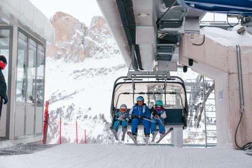 three people sitting on a ski lift in the snow at MyTime Hotels la Grotta in Vigo di Fassa