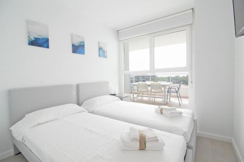 2 Betten in einem weißen Zimmer mit einem Tisch in der Unterkunft Global Properties, Apartamento con terraza, vistas al mar y a la piscina in Canet d'en Berenguer