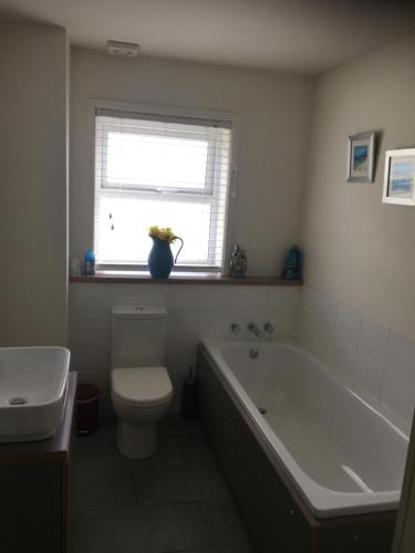 a bathroom with a toilet and a tub and a window at The Corner House in Halesworth