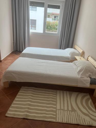 two beds in a room with a window and a rug at Sea view malabata family only in Tangier