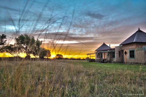a building in a field with the sunset in the background at Emoya Basotho Lodge in Bloemfontein