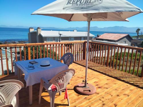a table and chairs on a deck with an umbrella at Pêrel of Perlemoenbaai in Gansbaai