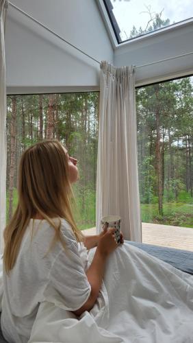a woman sitting in bed looking out a window at WUUD Pädaste in Simisti