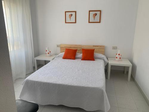1 dormitorio con 1 cama con almohadas de color naranja y 2 mesas en Piso vacacional con piscina en Benicassim, en Benicàssim