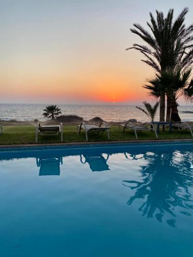 a swimming pool with a view of the ocean at sunset at Kymmates Beach Front Villas in Paphos City