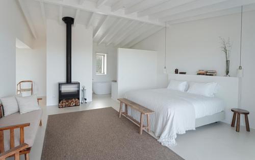 a white bedroom with a large bed and a fireplace at Amaria in Aljezur