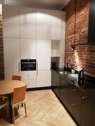 a kitchen with white cabinets and a table and a brick wall at Apartamenty Carskie Koszary in Zamość