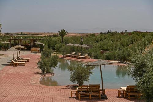 a pool of water with tables and umbrellas and chairs at Le Parc des Oliviers in Marrakech