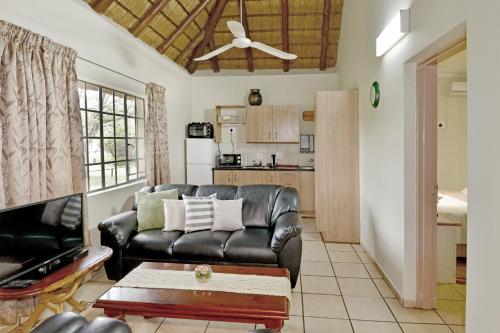 a living room with a leather couch and a kitchen at Komati River Chalets in Komatipoort