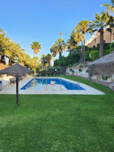 a swimming pool with an umbrella and some palm trees at DELUXE Studio ATHOS 50 MP Garden patio BENALMADENA Golf & Beach in Benalmádena