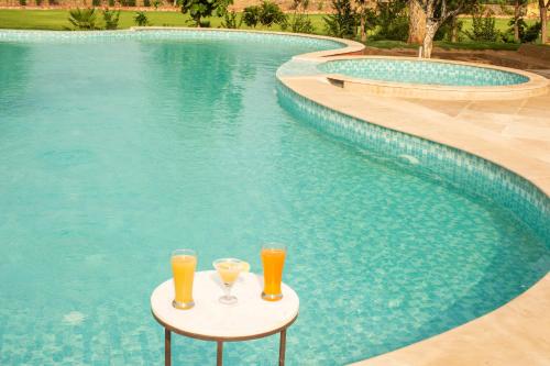 two glasses of orange juice on a table next to a swimming pool at Ratan Villas Sariska in Alwar