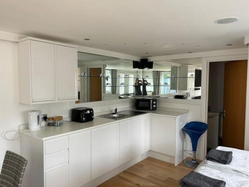 a kitchen with white cabinets and a blue stool at Cosy Studio Cabin with Optional Hot Tub Lilliput near Sandbanks beach in Poole
