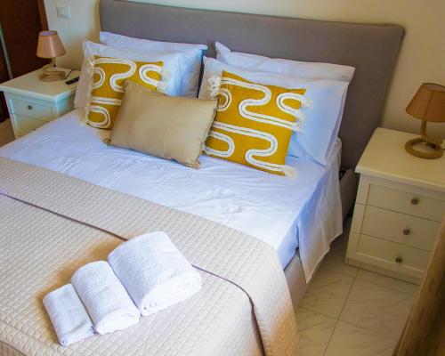 Cama blanca con almohadas y toallas amarillas y blancas en Roussev Apartment - Coastal Gem - Anzio, en Anzio