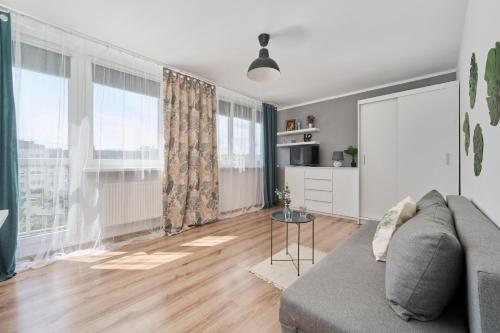 a living room with a gray couch and large windows at Studio with Sky Tower View Wrocław by Renters in Wrocław