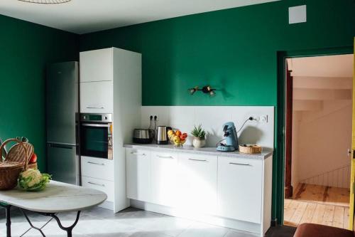 une cuisine avec des murs verts, des armoires blanches et une table dans l'établissement Gîte Trou Life, à Bozouls