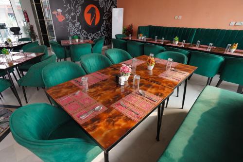a dining room with a wooden table and green chairs at Hotel Orange One in Lahore