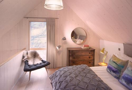 een slaapkamer met een bed en een stoel op zolder bij Eastside Woodshed - Pentland cabin set in the hills near Edinburgh in Penicuik
