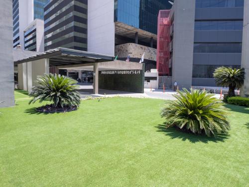 a green lawn in front of a building with palm trees at Krystal Urban Monterrey San Jeronimo in Monterrey