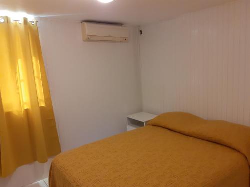 - une petite chambre avec un lit et un rideau jaune dans l'établissement La verdure, au Gosier