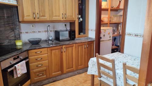 cocina con armarios de madera, microondas y mesa en CASA BERELY, en Cariño