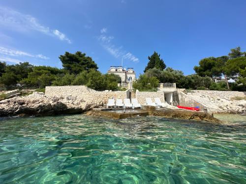 a house in the water with chairs in front at Luxury Seaside Villa with a classic Mediterranean Olive Garden, a fully equipped Professional Kitchen, Pool, Sauna, Padle Boards and Canoe - Miolin Beach House in Trogir