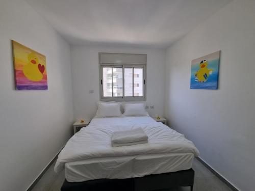 a bed in a room with two paintings on the wall at Ducks on the beach in ‘Akko