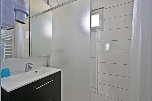 La salle de bains blanche est pourvue d'un lavabo et d'un miroir. dans l'établissement LE PETIT BONHEUR - PLACE PARKING PRIVEE - CLiM - TERRASSE - PISCINE PARTAGEE - PROCHE PARC SPIROU, à Saint-Saturnin-les-Avignon