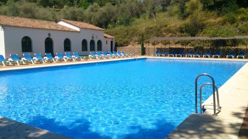 a swimming pool with blue chairs and a building at Finca Valbono Apartamentos Rurales y Hotel in Aracena
