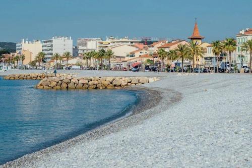 a beach with a group of buildings and palm trees at Appartement bord de mer « La Petite Ma-Line » in Cagnes-sur-Mer