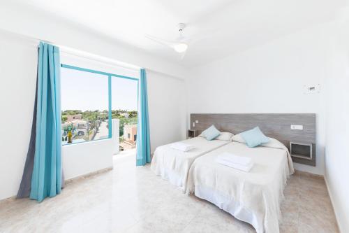 um quarto branco com 2 camas e uma grande janela em Hostal Cala Llombards em Cala Llombards