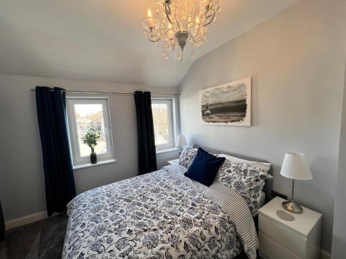 a bedroom with a bed and a chandelier and two windows at Luxury Retreat Beach House - Sleeps 6 in Southend-on-Sea