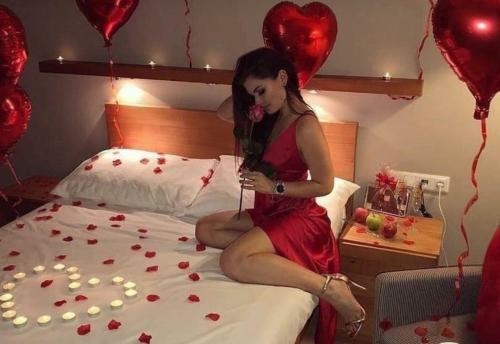 Una mujer con un vestido rojo sentada en una cama con corazones en Departamento para parejas, en Guayaquil