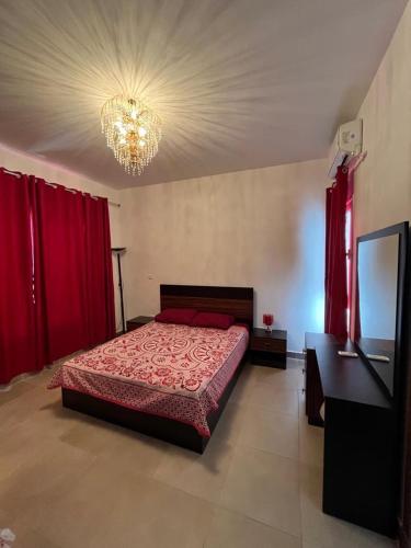 a bedroom with a bed with red curtains and a chandelier at amwaj in Dawwār Ruḩayyim