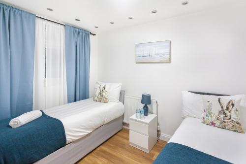 two beds in a small room with blue curtains at Holloway Budget Apartment - 1 Minute to Emirates Stadium - Next to Station - City Center in London
