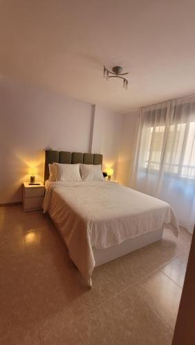 a white bedroom with a large bed and a window at Apartamento Sol y Mar in Sant Carles de la Ràpita