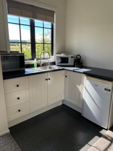 a kitchen with white cabinets and a sink and a microwave at The Barn in Mosgiel