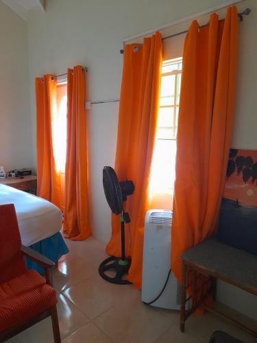 Habitación con cortinas de color naranja, cama y ventana en Alexander's Apartment Carriacou, en Carriacou