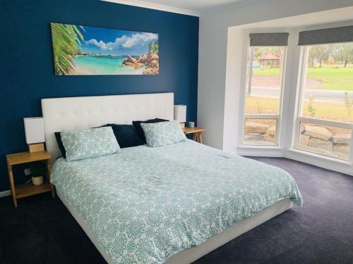 a bedroom with a bed with blue walls and windows at Sea & Vines in McLaren Flat