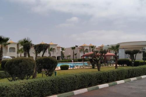 a resort with a pool and palm trees and buildings at Joli Appartement à Mozona Beach 2, Sidi Rahal in Dar Hamida
