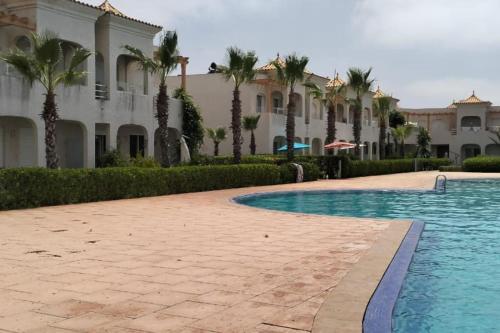 a resort with a swimming pool and palm trees at Joli Appartement à Mozona Beach 2, Sidi Rahal in Dar Hamida