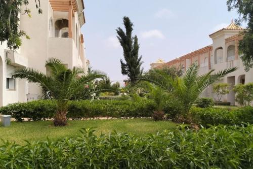 a garden in front of a building with palm trees at Joli Appartement à Mozona Beach 2, Sidi Rahal in Dar Hamida