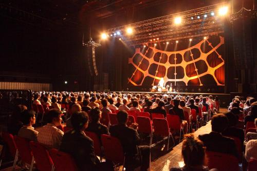a crowd of people in an auditorium watching a stage at Shinagawa Prince Hotel in Tokyo