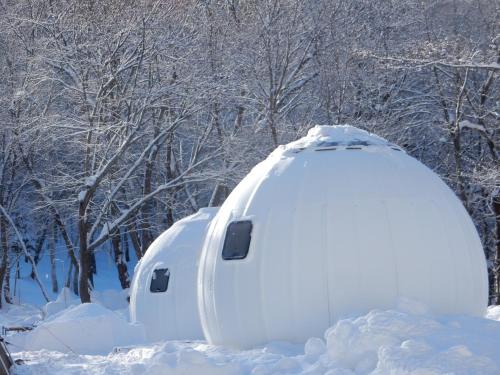 deux maisons igloo couvertes de neige devant des arbres dans l'établissement Redoor Sapporo, à Sapporo